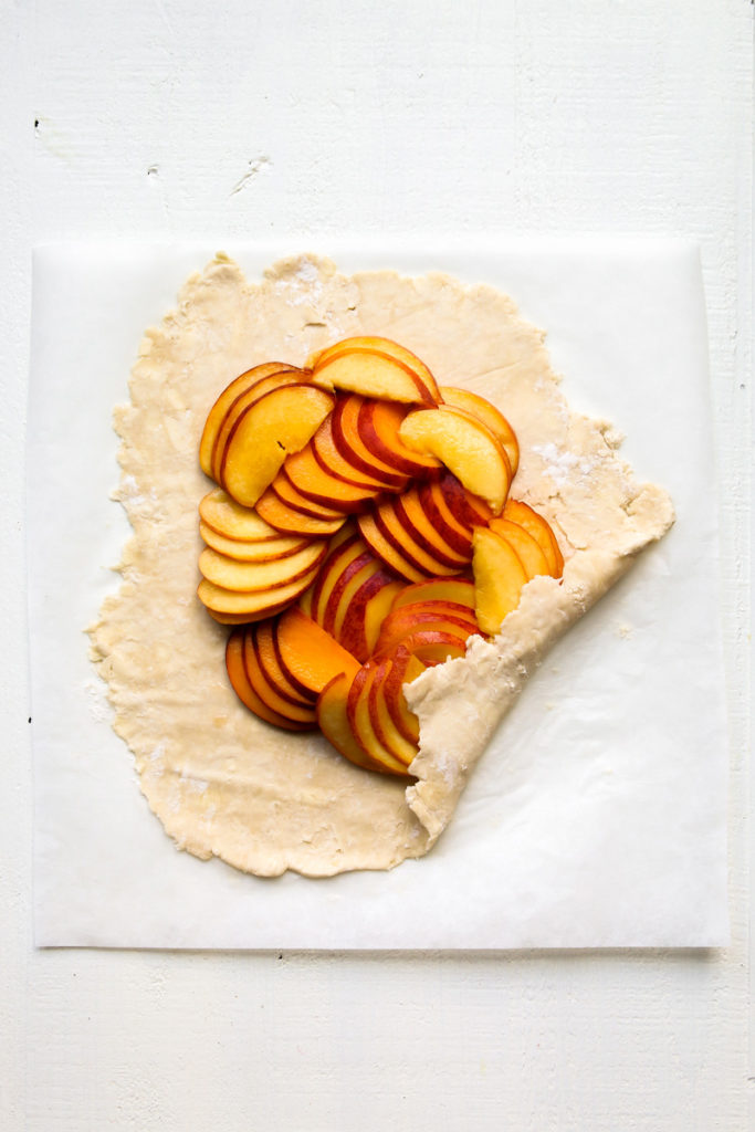 Pie crust filled with sliced peaches on parchment paper.