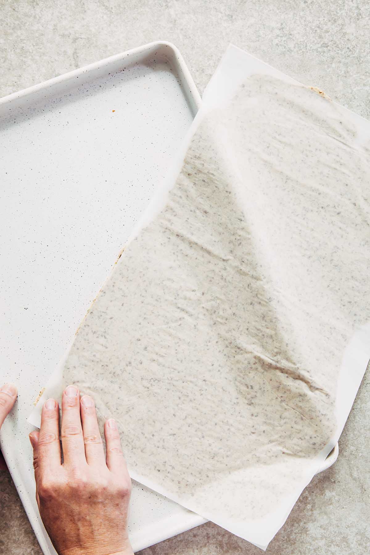 Hands transferring rolled dough between pieces of parchment paper onto a white baking sheet.
