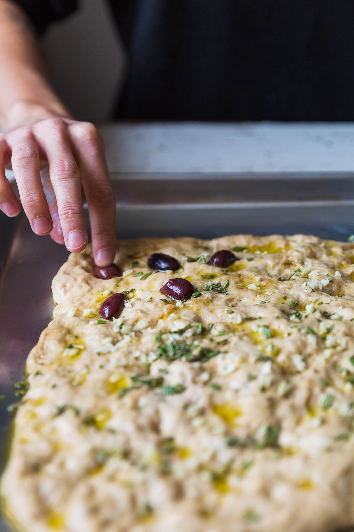 Woman's hand pressing olives into an unbaked focaccia.