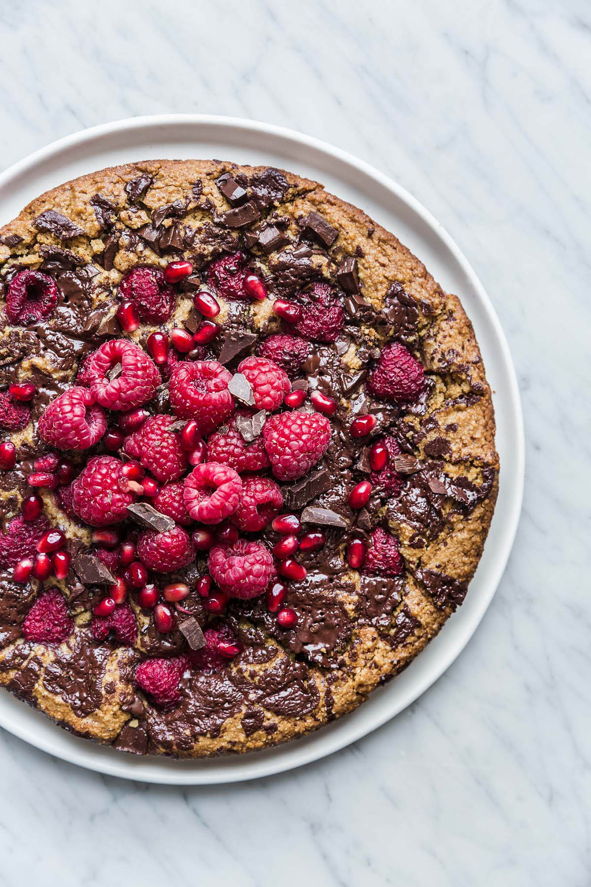 A large almond chocolate cake topped with raspberries on a plate.