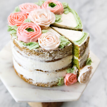 Layer cake with buttercream roses decorating, on marble cake stand, one slice cut.