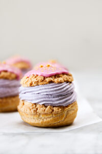 Cream puffed filled with purple cream and topped with pink glaze.