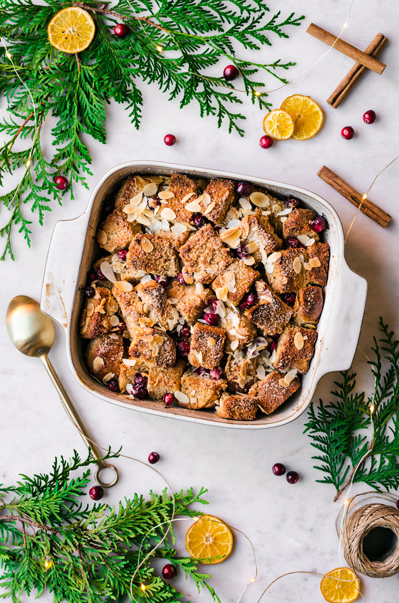 White wine bread pudding in a baking dish surrounded by greenery, oranges, and cinnamon sticks.