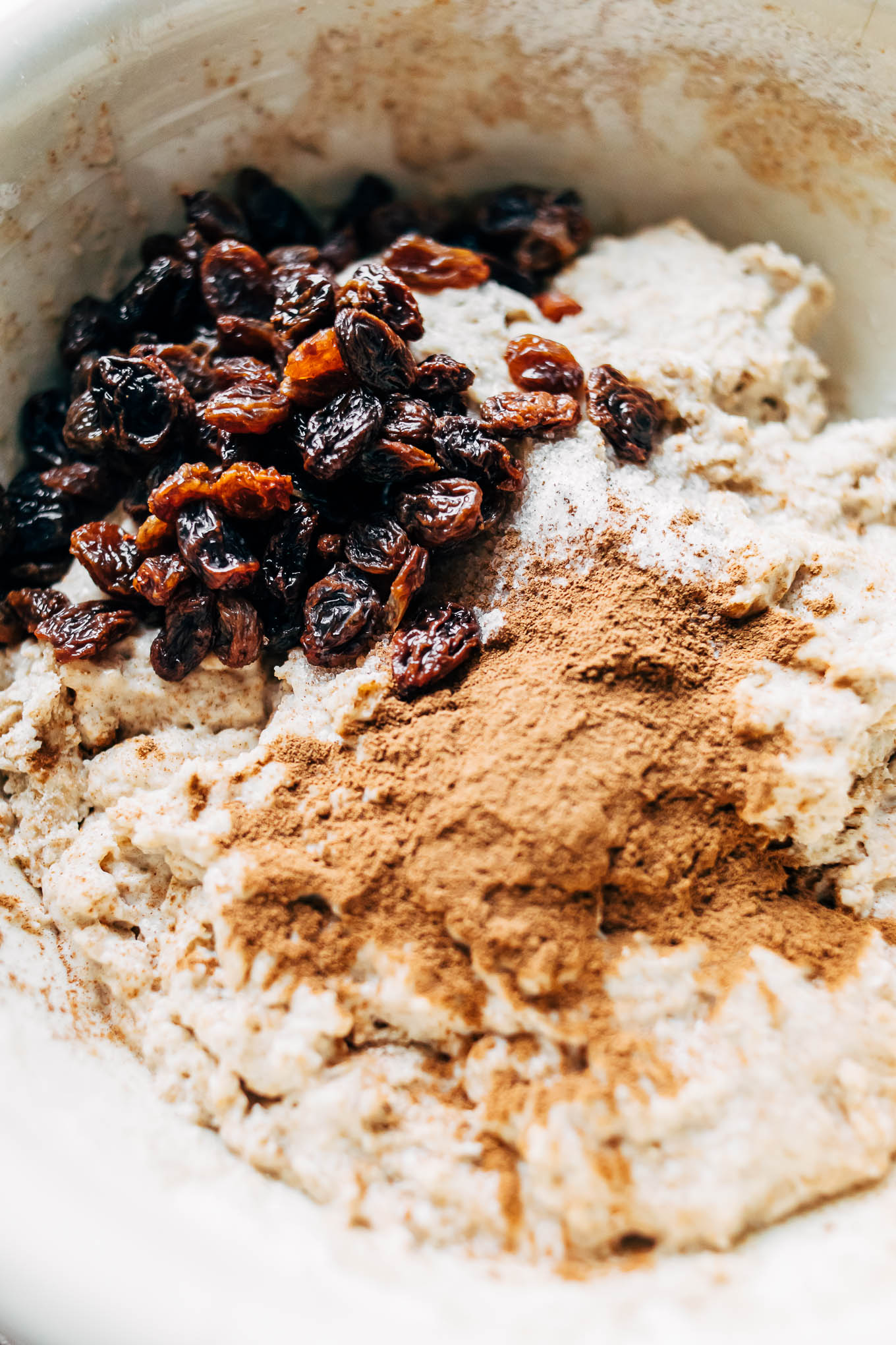 overhead close up image of a bowl flour, raisins and cinnamon.
