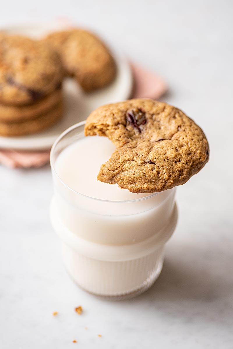 A cookie with a bite out of it sitting on the rim of a glass of milk.