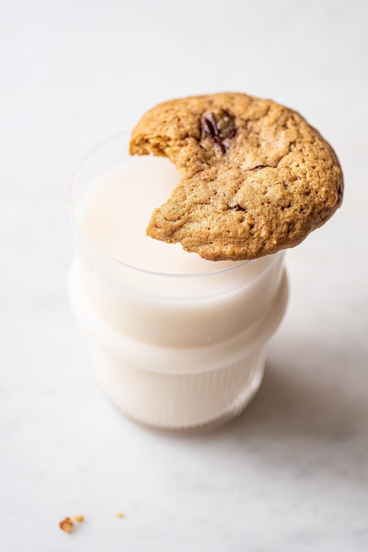 A chocolate chunk sourdough cookie with a bite out of it sitting on the rim of a glass of milk.