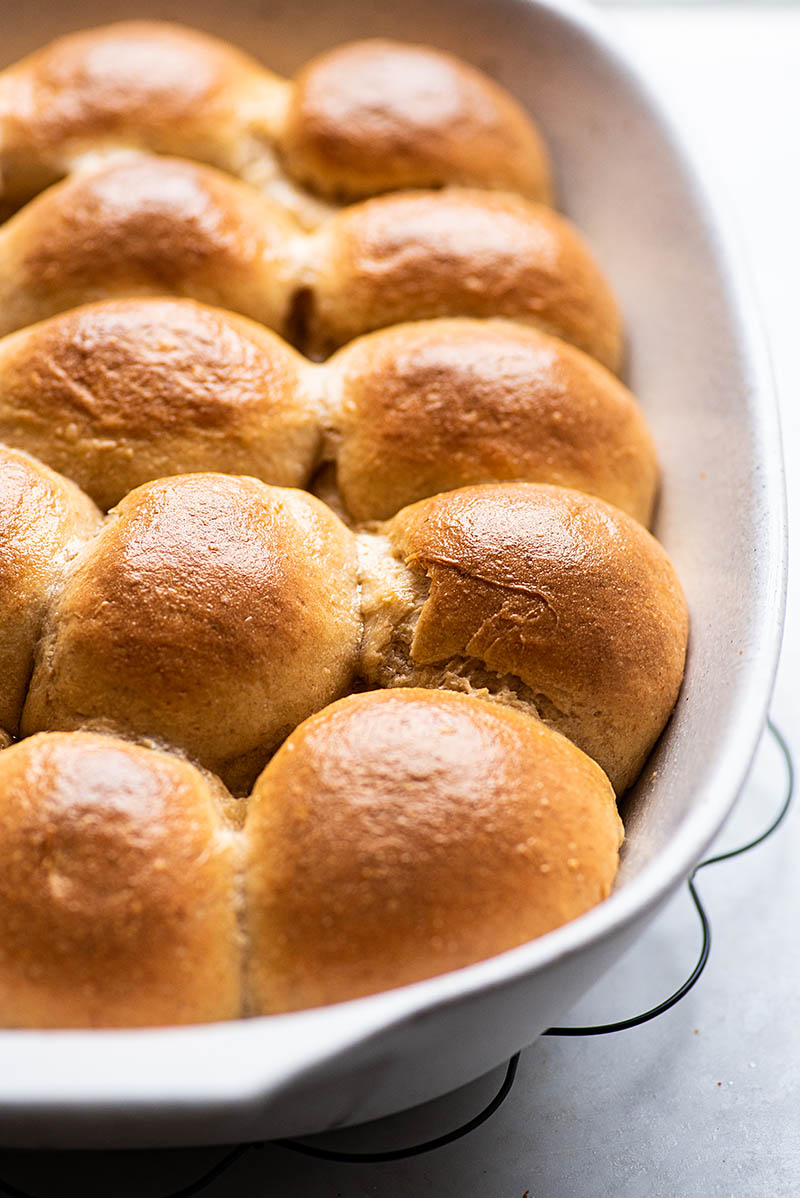 close up image of baked sourdough dinner rolls in a white baking pan.