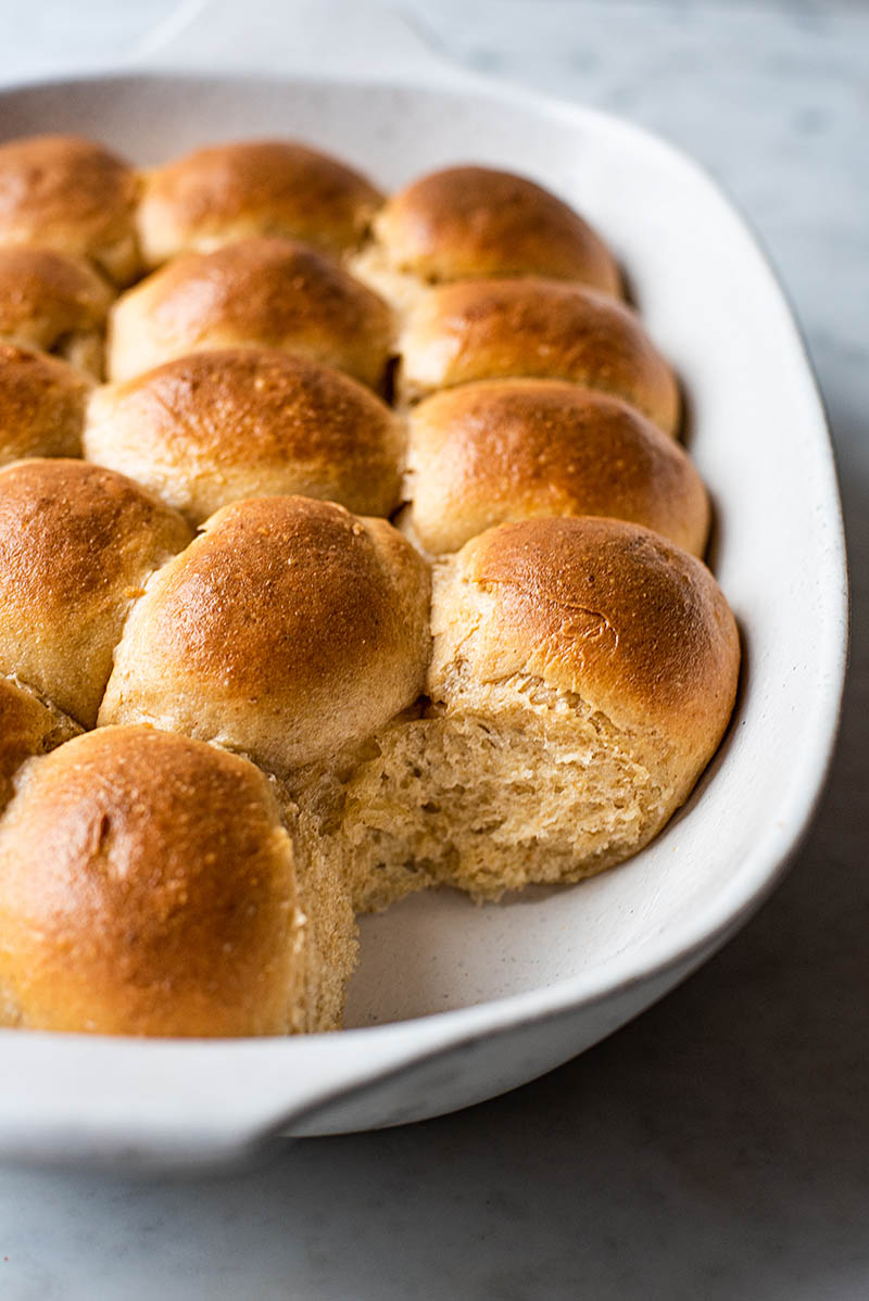 close up image of baked sourdough dinner rolls in a white baking pan.