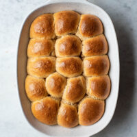 overhead image of baked sourdough dinner rolls in a white baking pan.