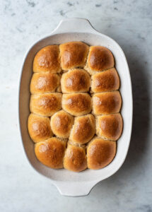 overhead image of baked sourdough dinner rolls in a white baking pan.