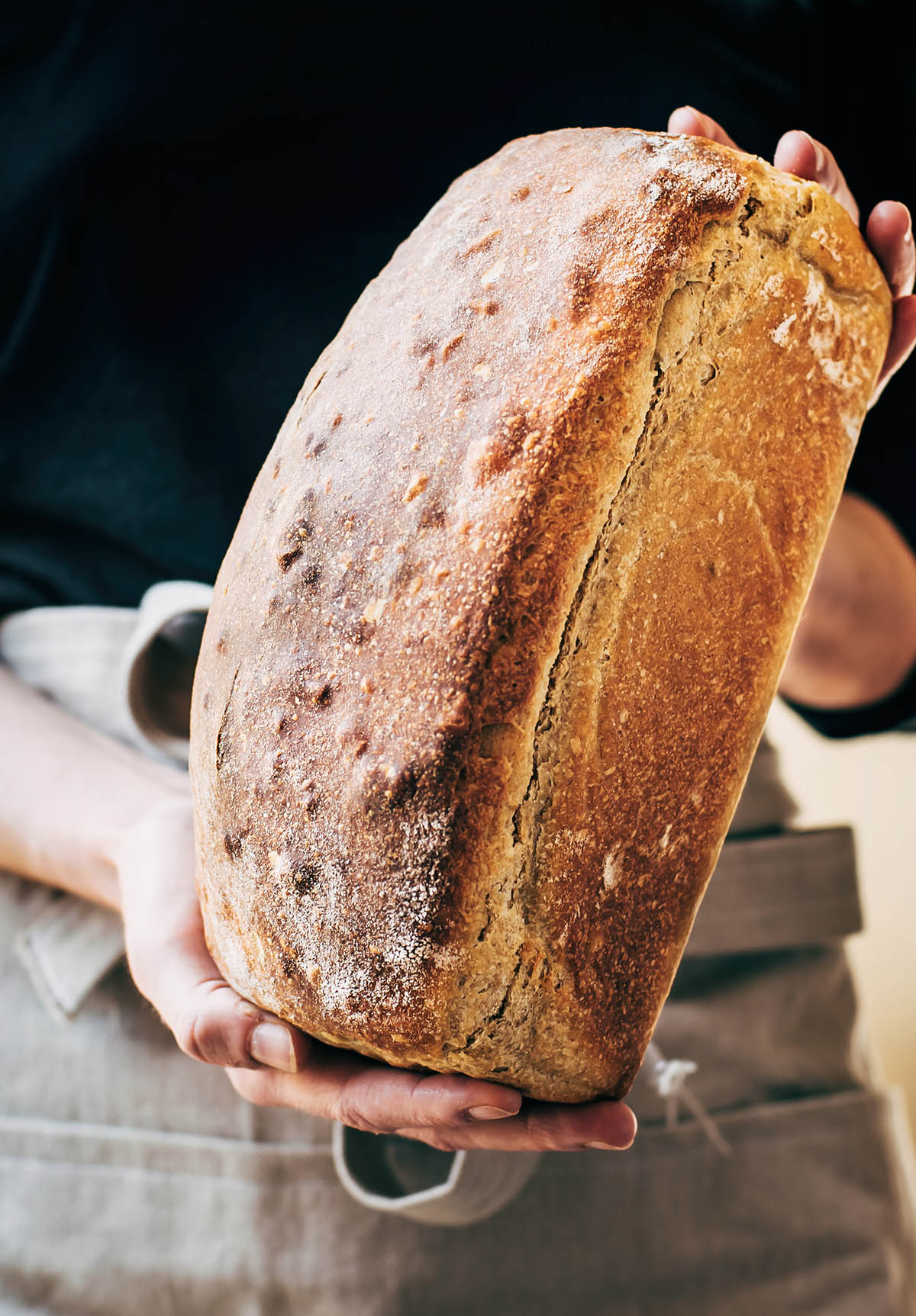 A woman's hands holding a loaf of sourdough sandwich bread.