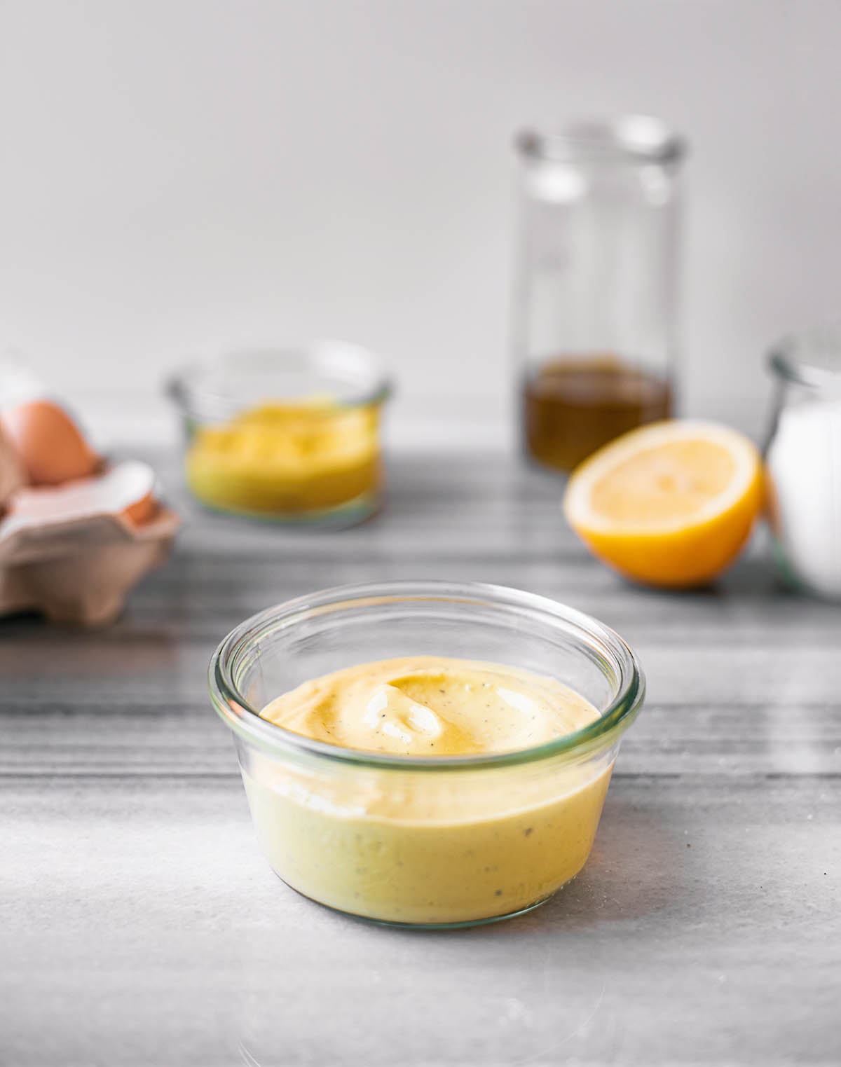 A small bowl of whole egg mayonnaise with ingredients in the background.