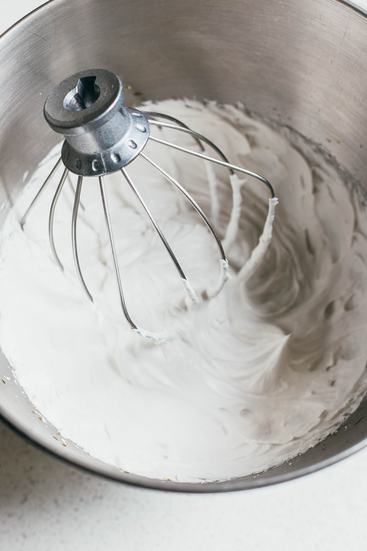 Whipped cream in a metal bowl with the mixing attachment in the bowl.