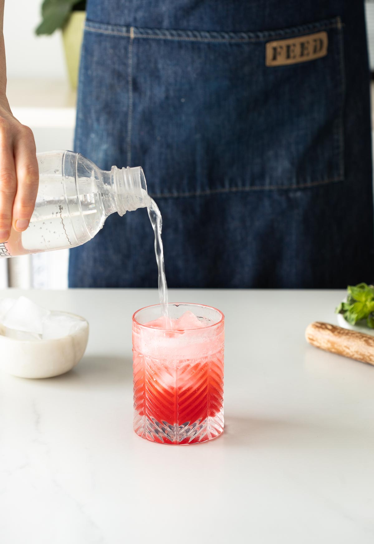 Soda water being poured into a pink cocktail.