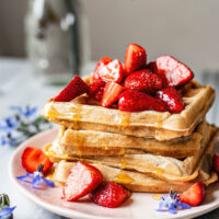 Stack of square waffles topped with strawberries.