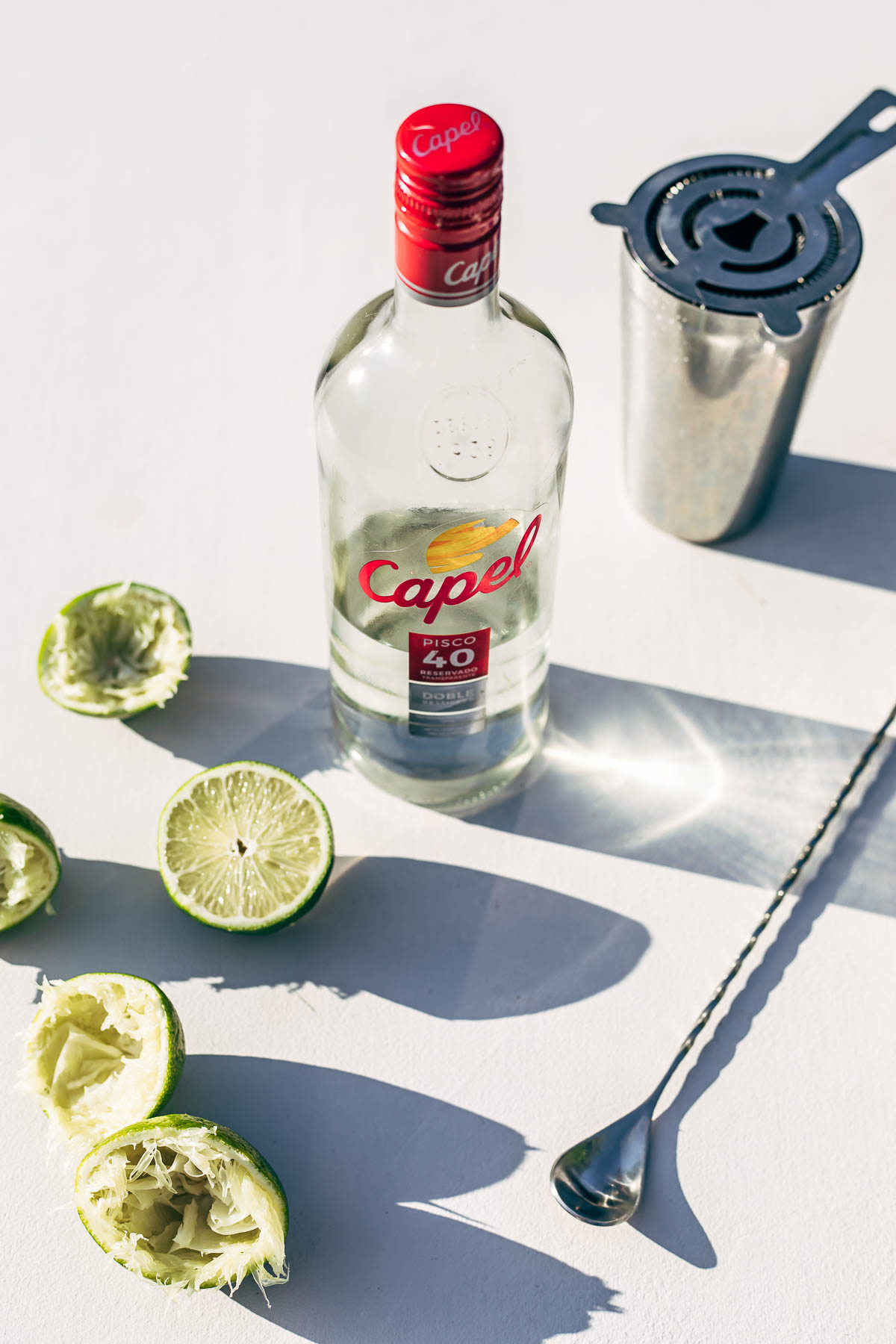 A bottle of Pisco on a white surface surrounded by cut limes.