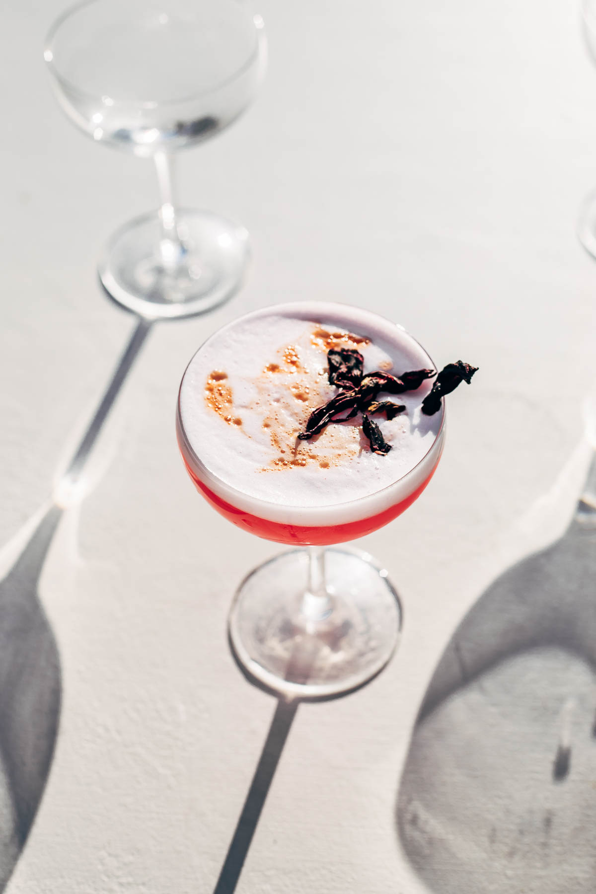 A hibiscus sour cocktail in the sun on a white surface.