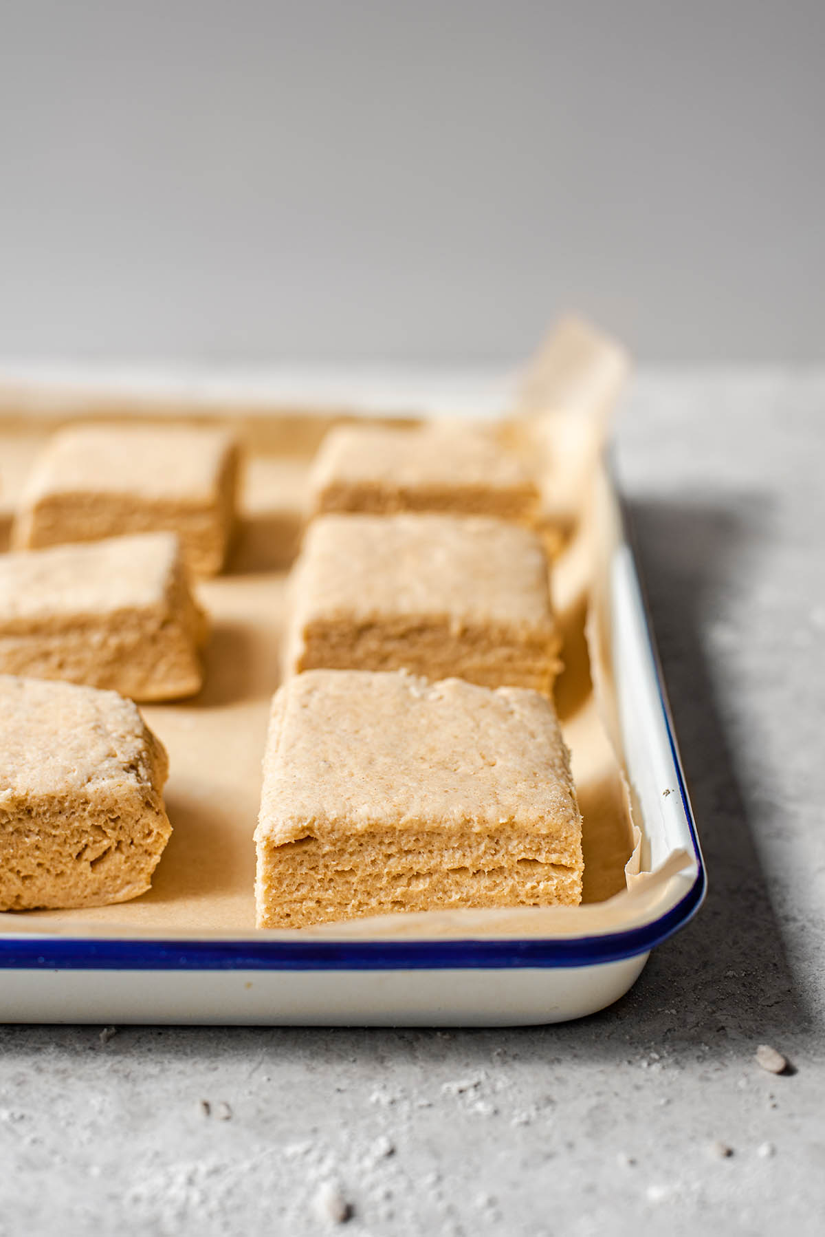Several square biscuits, unbaked, on a baking sheet with parchment paper.
