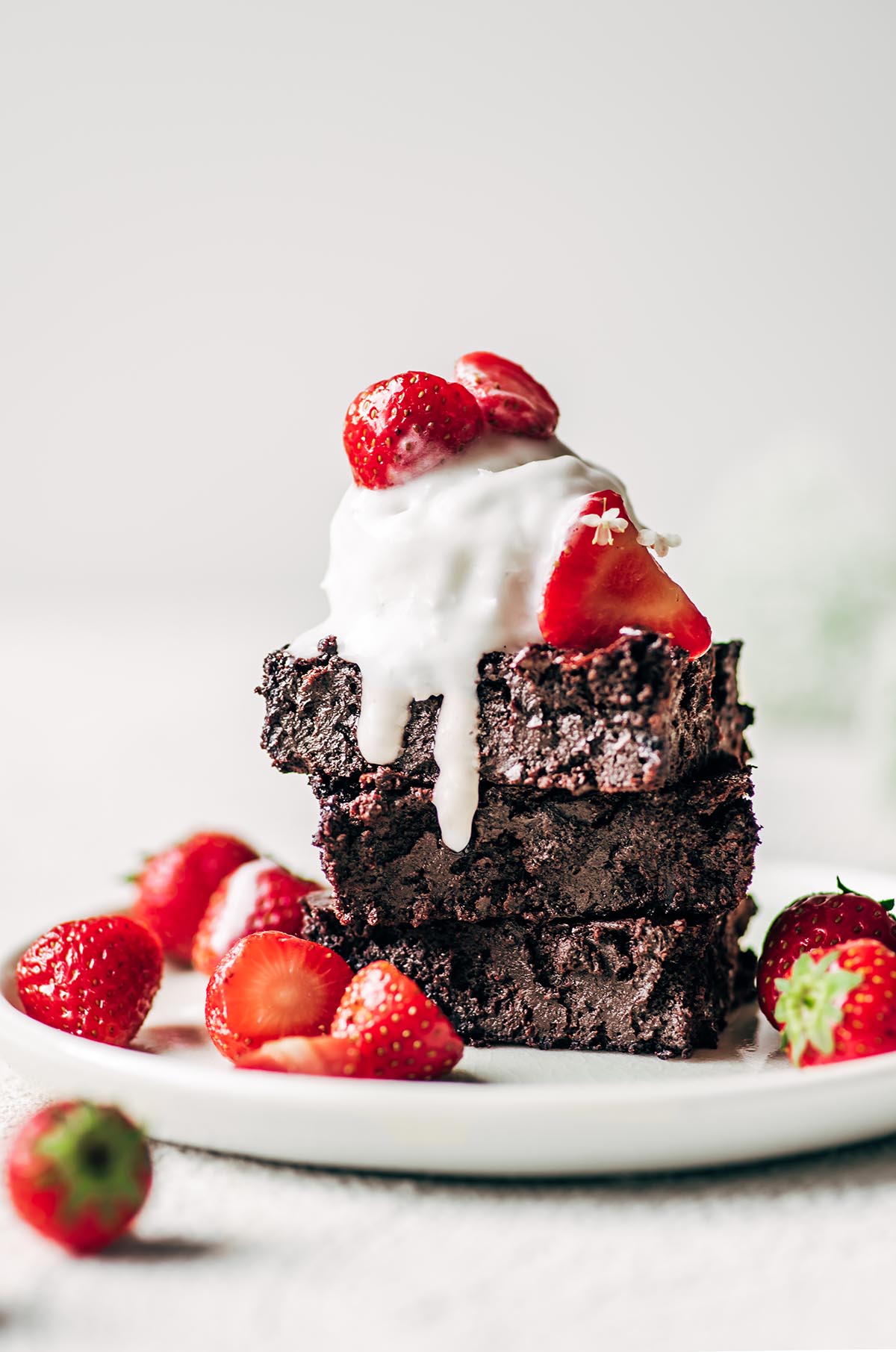 Three brownies stacked on a plate with ice cream and strawberries.