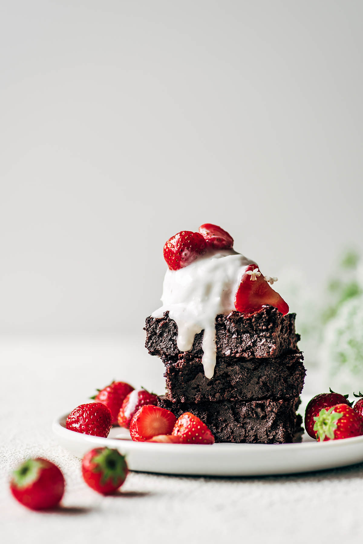 Three brownies stacked on a plate with ice cream and strawberries.