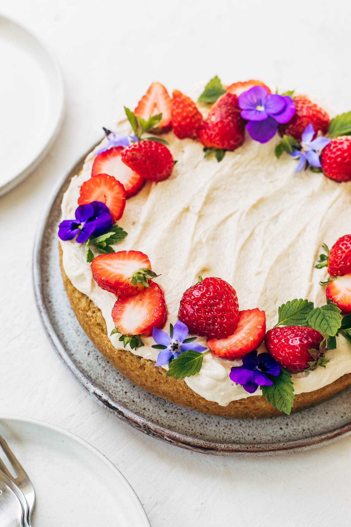 A round white cake topped with buttercream and a circle of strawberries and edible flowers.