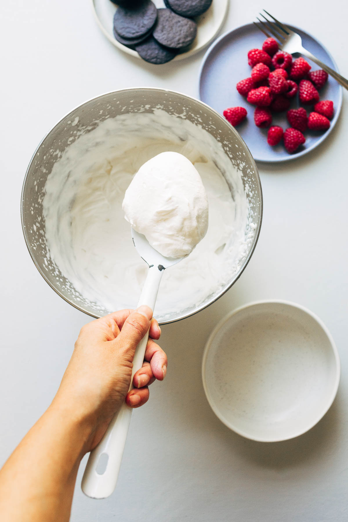 Woman's hand holding up a large spoonful of whipped cream from a large bowl.
