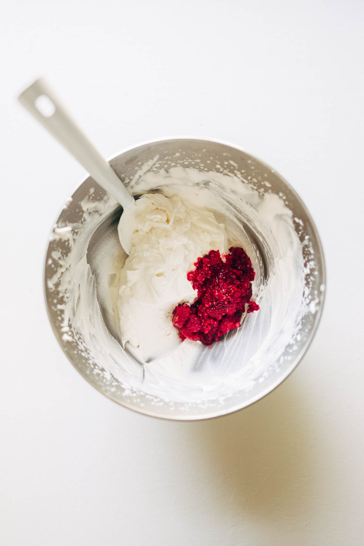 Mashed raspberries in a large bowl of whipped cream.