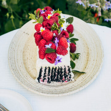 Icebox cake topped with berries and flowers, one slice removed.