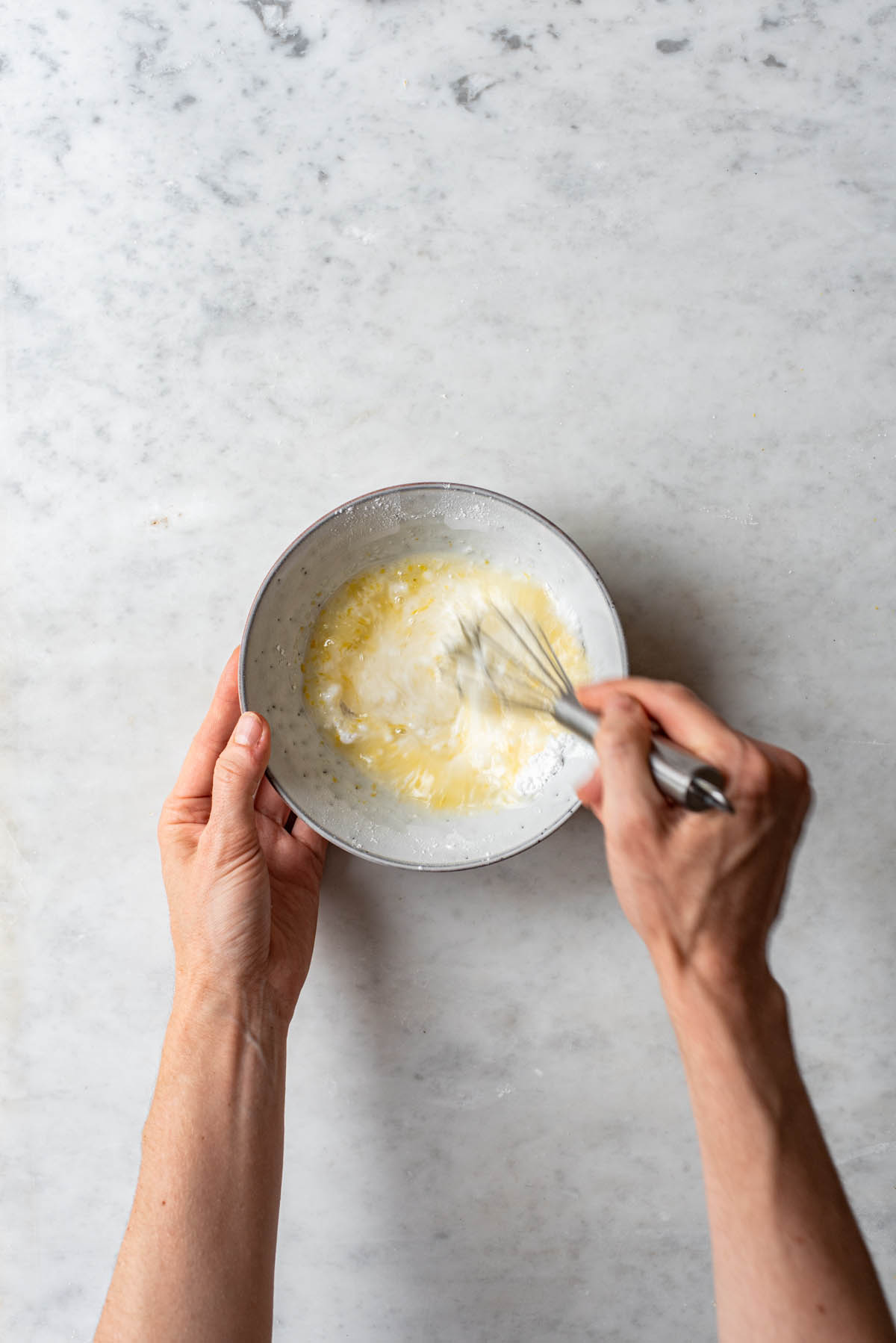 A hand whisking lemon glaze in a small grey bowl.
