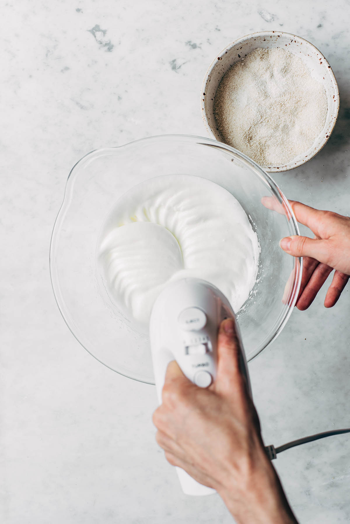 Hands using a hand mixer to whip meringue.