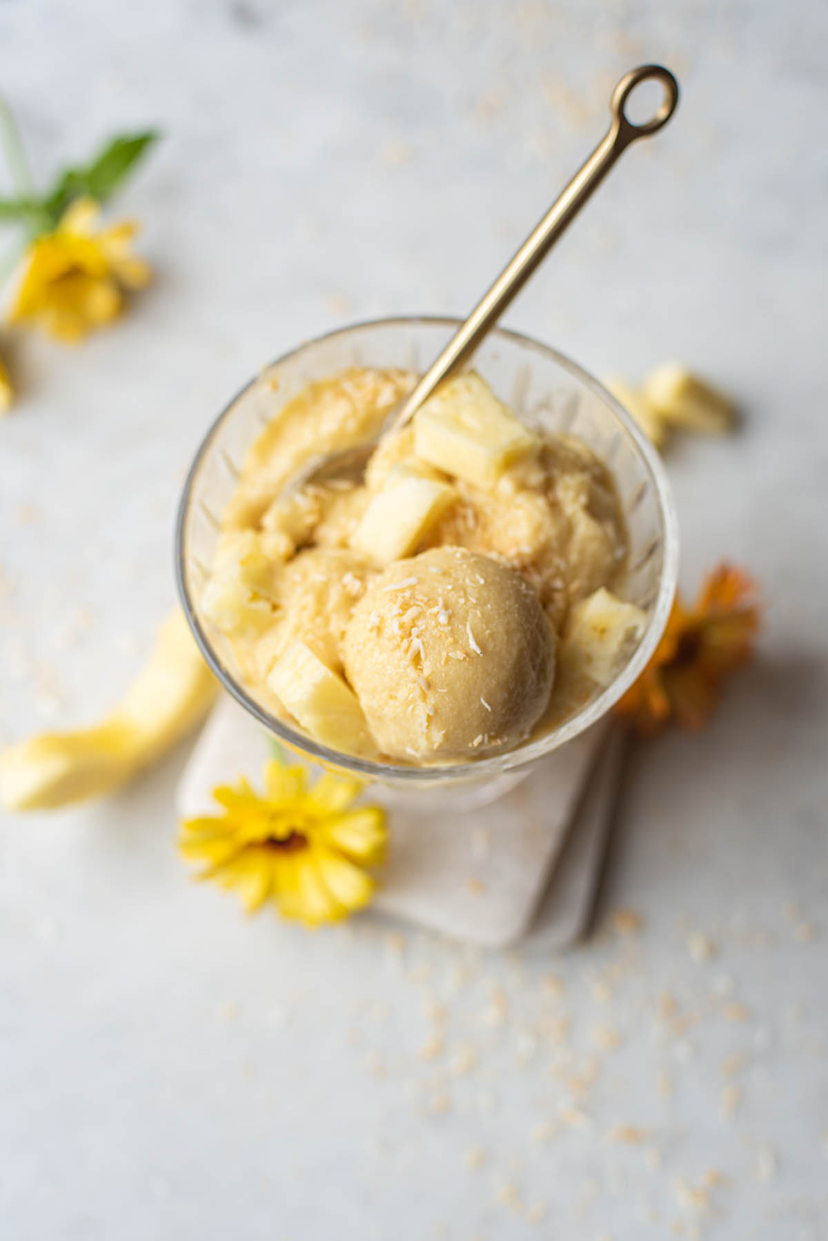 A dish of ice cream with a gold spoon and yellow flowers.