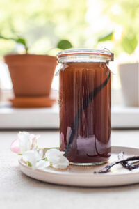 A jar of homemade vanilla syrup on a white plate in front of a window.