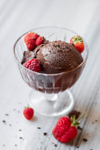 A scoop of chocolate vegan sherbet in a small glass pedestal bowl garnished with berries.