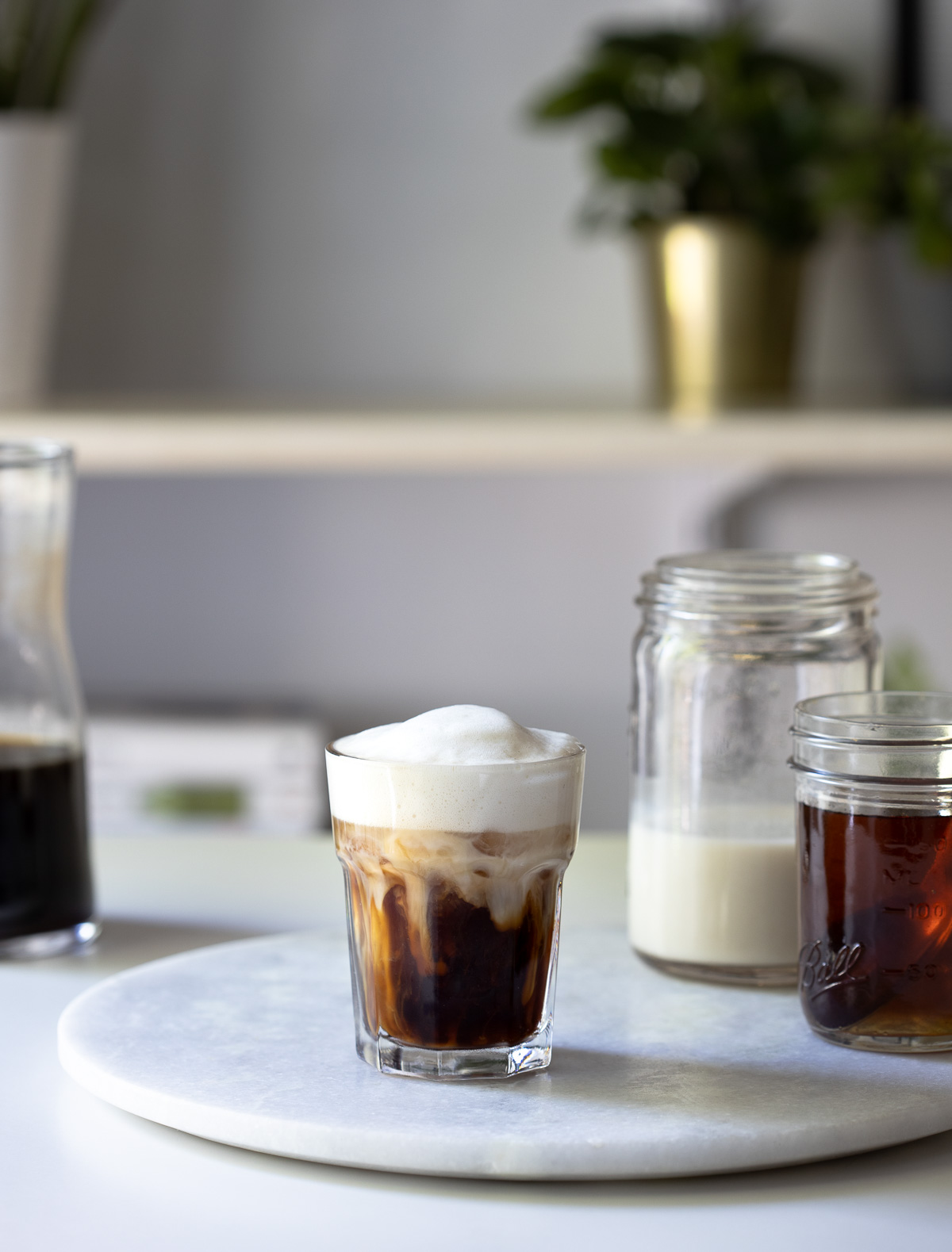 An iced vanilla latte on a round marble board next to jars of ingredients.