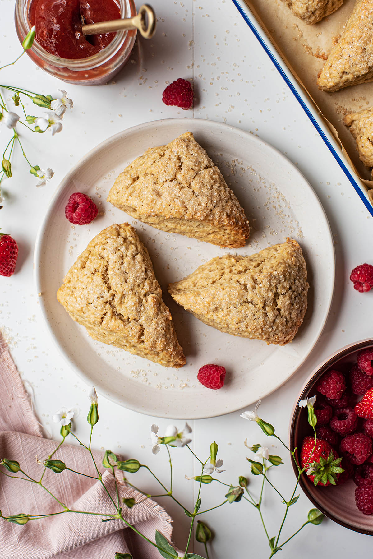 Three scones on a plate with raspberries.