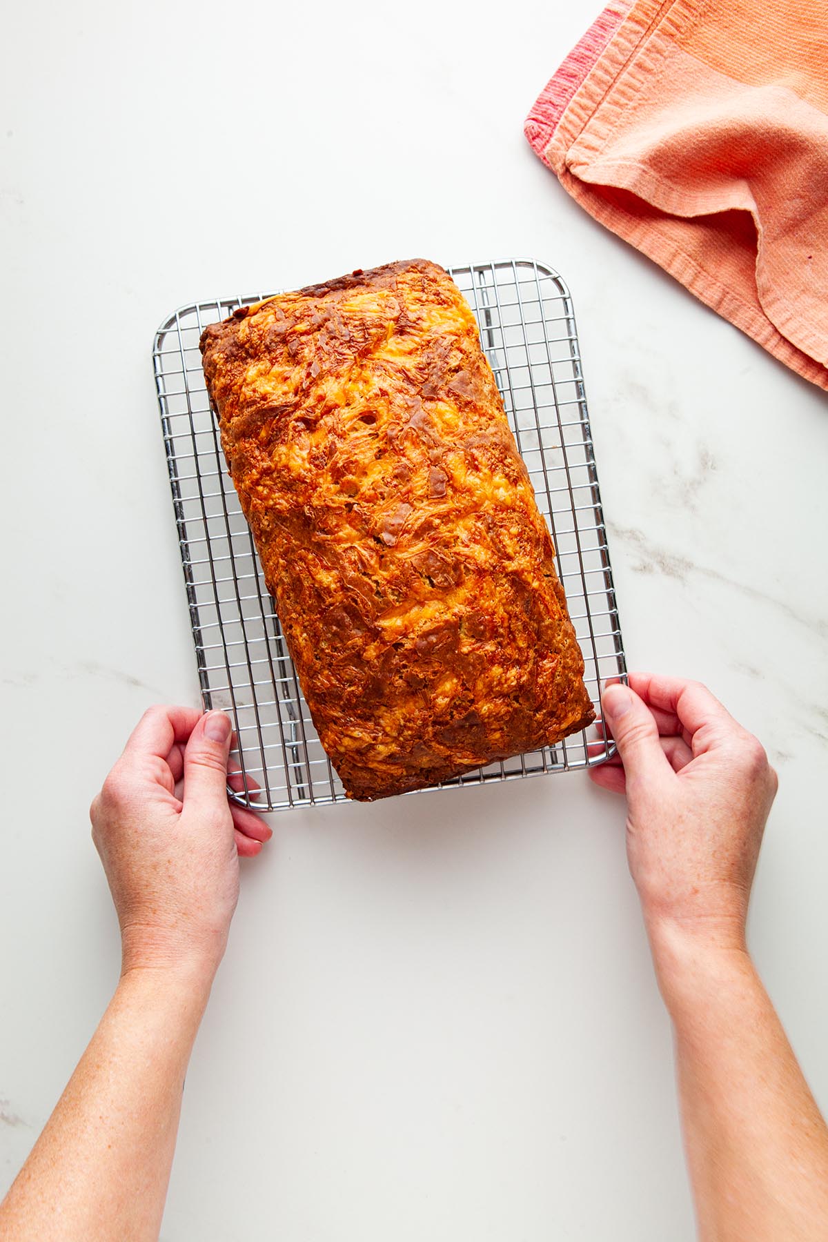 A hand holding the sides of a cooling rack with a baked loaf on top.