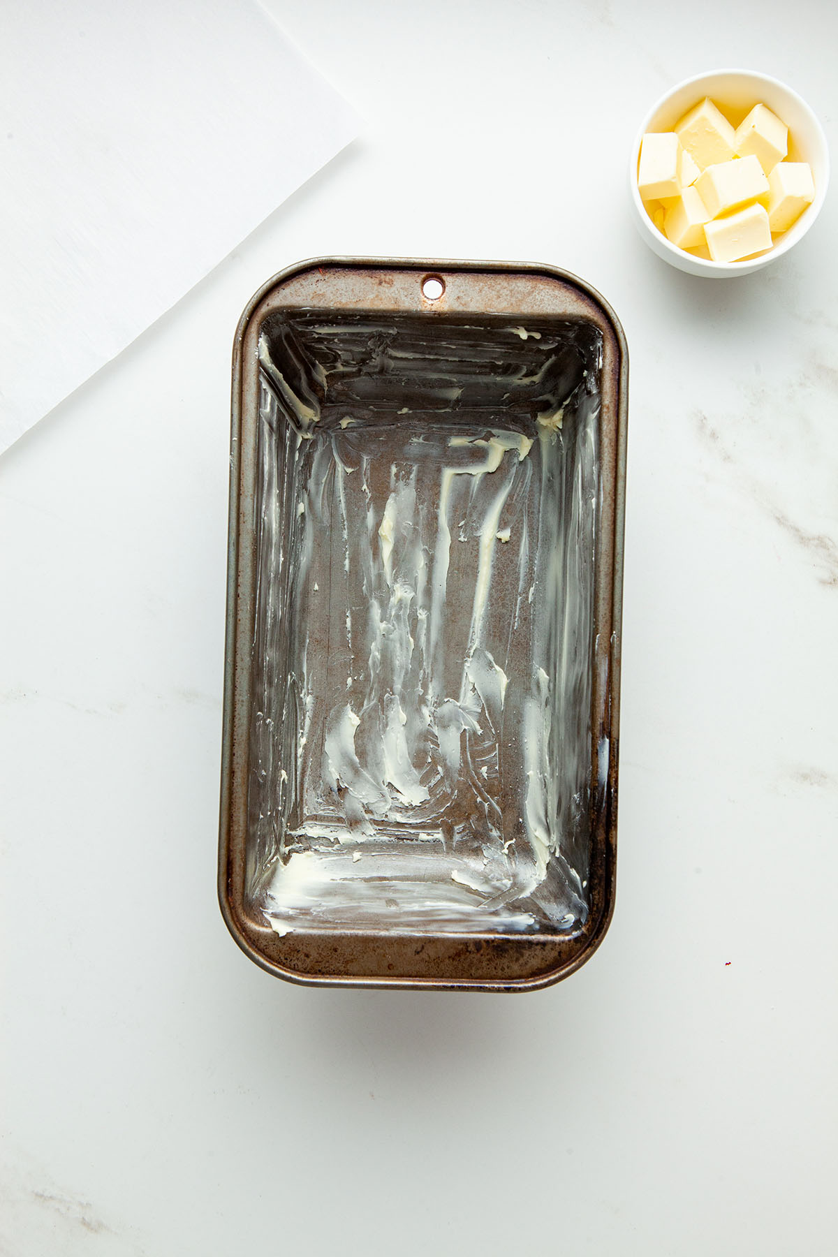 A buttered loaf tin on a marble surface.