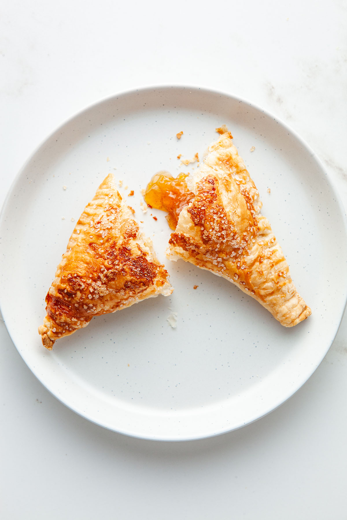 A puff pastry turnover split in half on a plate with jam oozing out.