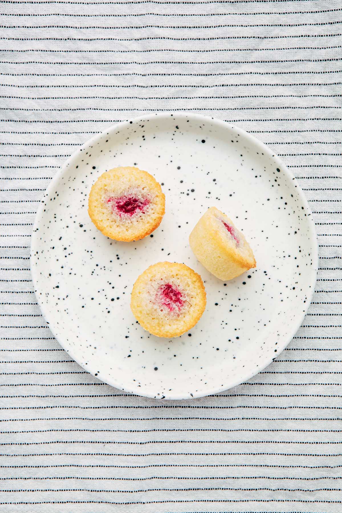 Three raspberry financiers on a speckled plate.