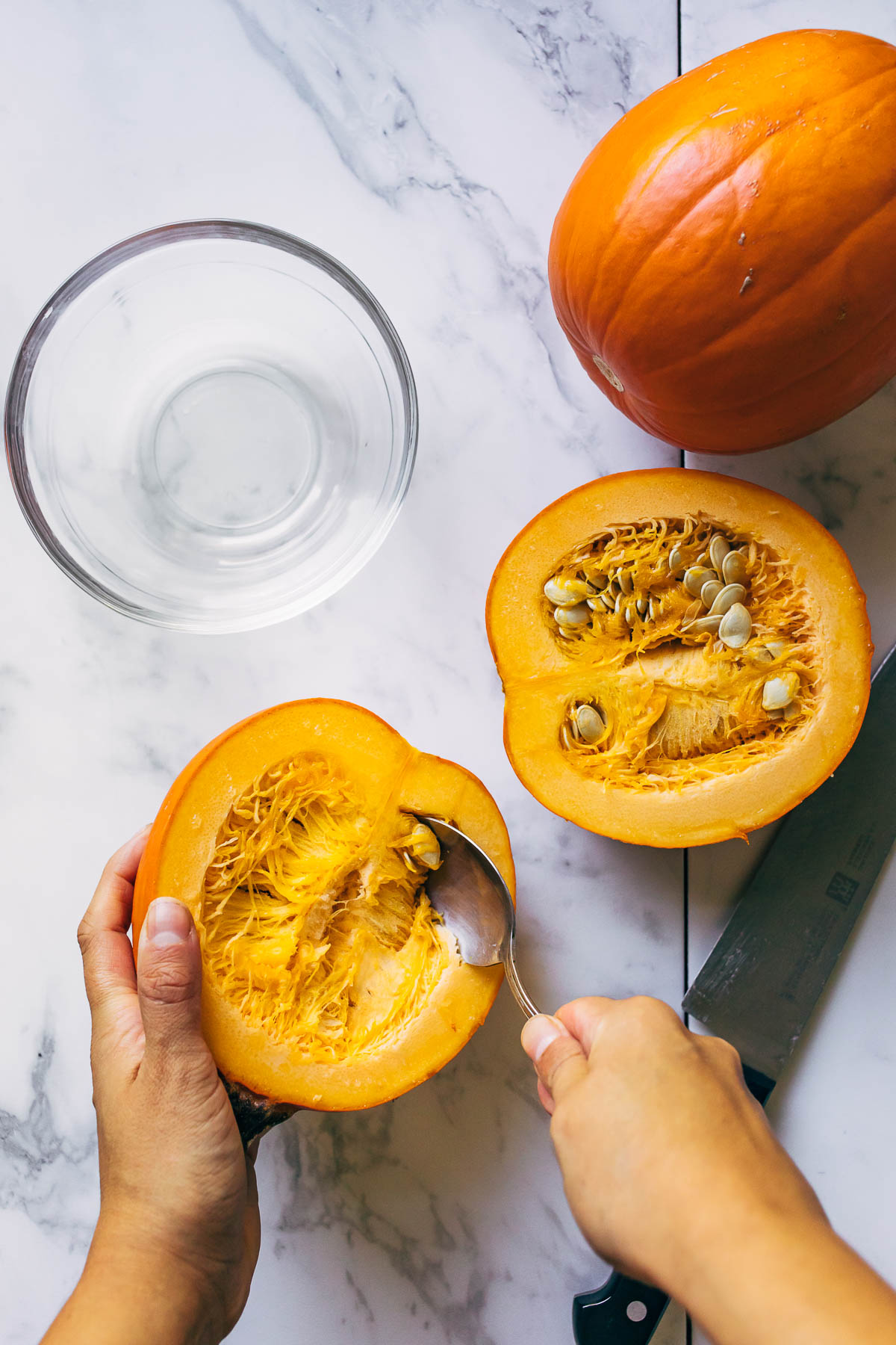 A hand scooping seeds out of a small pumpkin with a spoon.