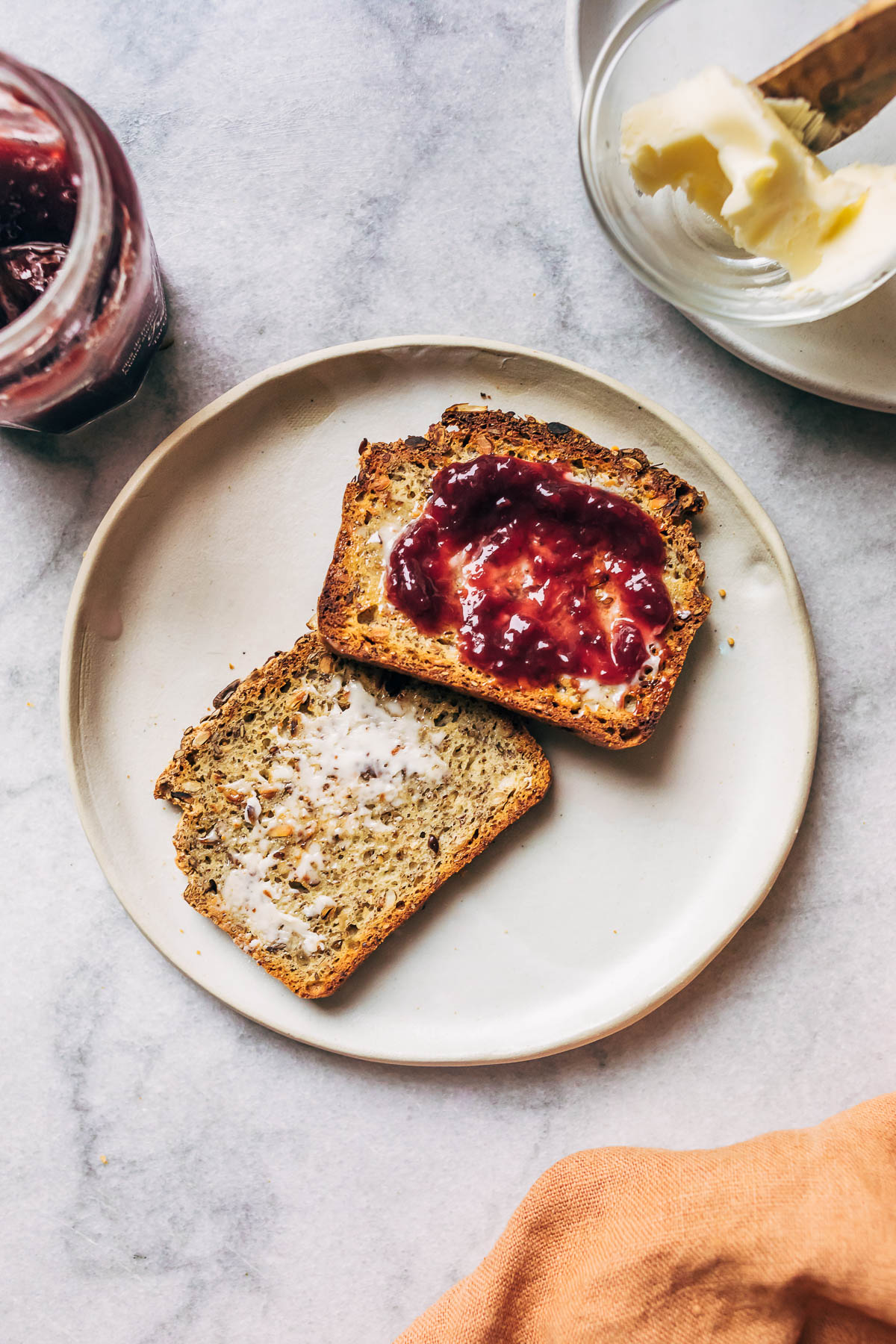 Two pieces of toast on a plate, one with butter and one with jam.