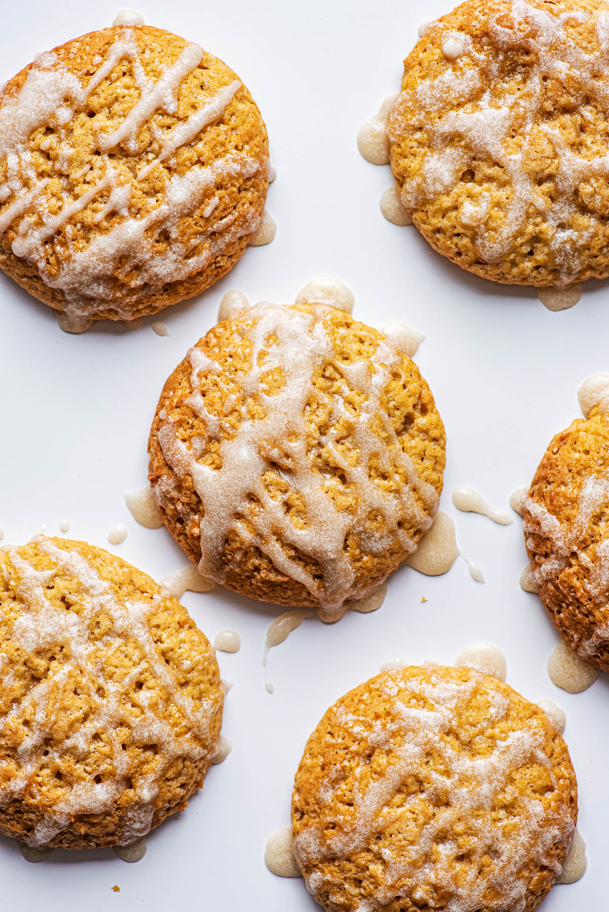 Six pumpkin cookies on a white background with glaze drizzles.