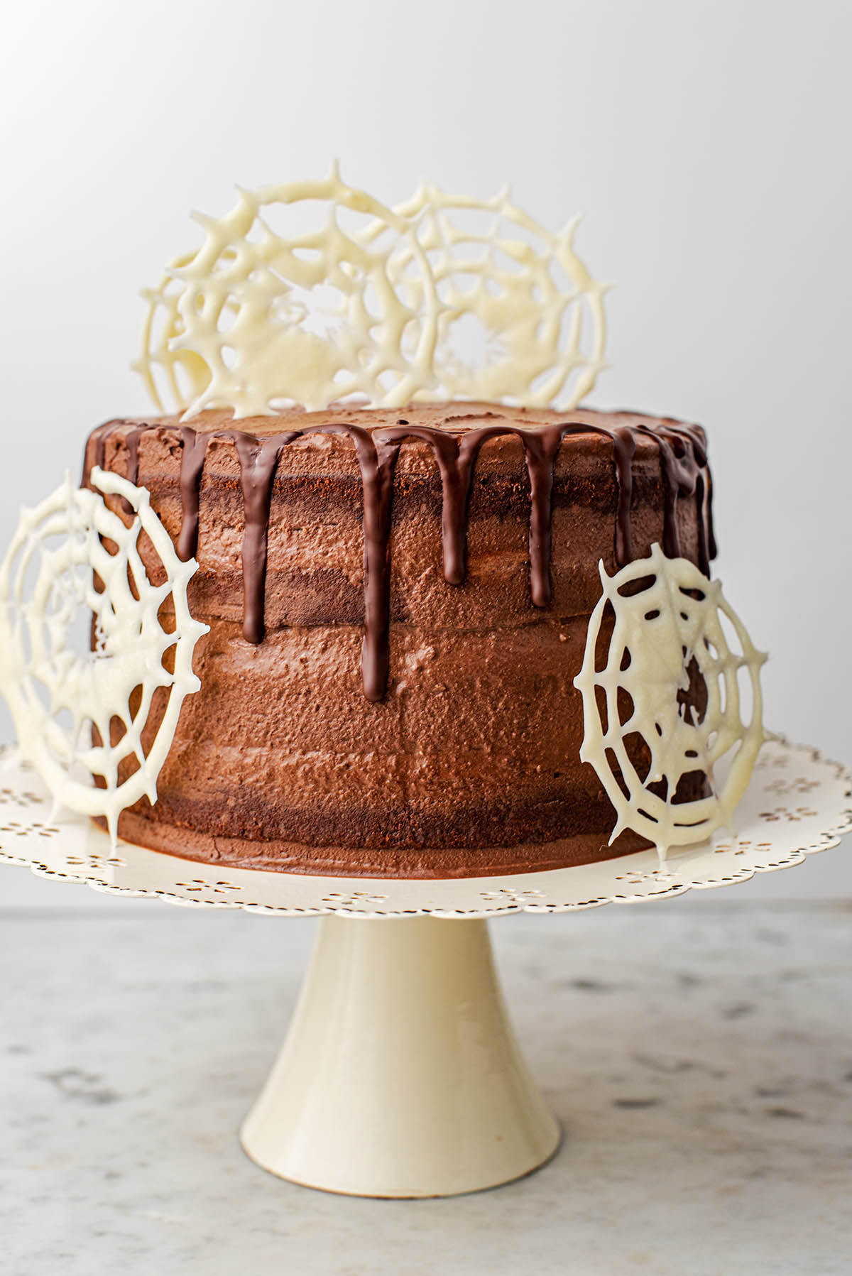 A large chocolate layer cake with white chocolate spiderwebs.
