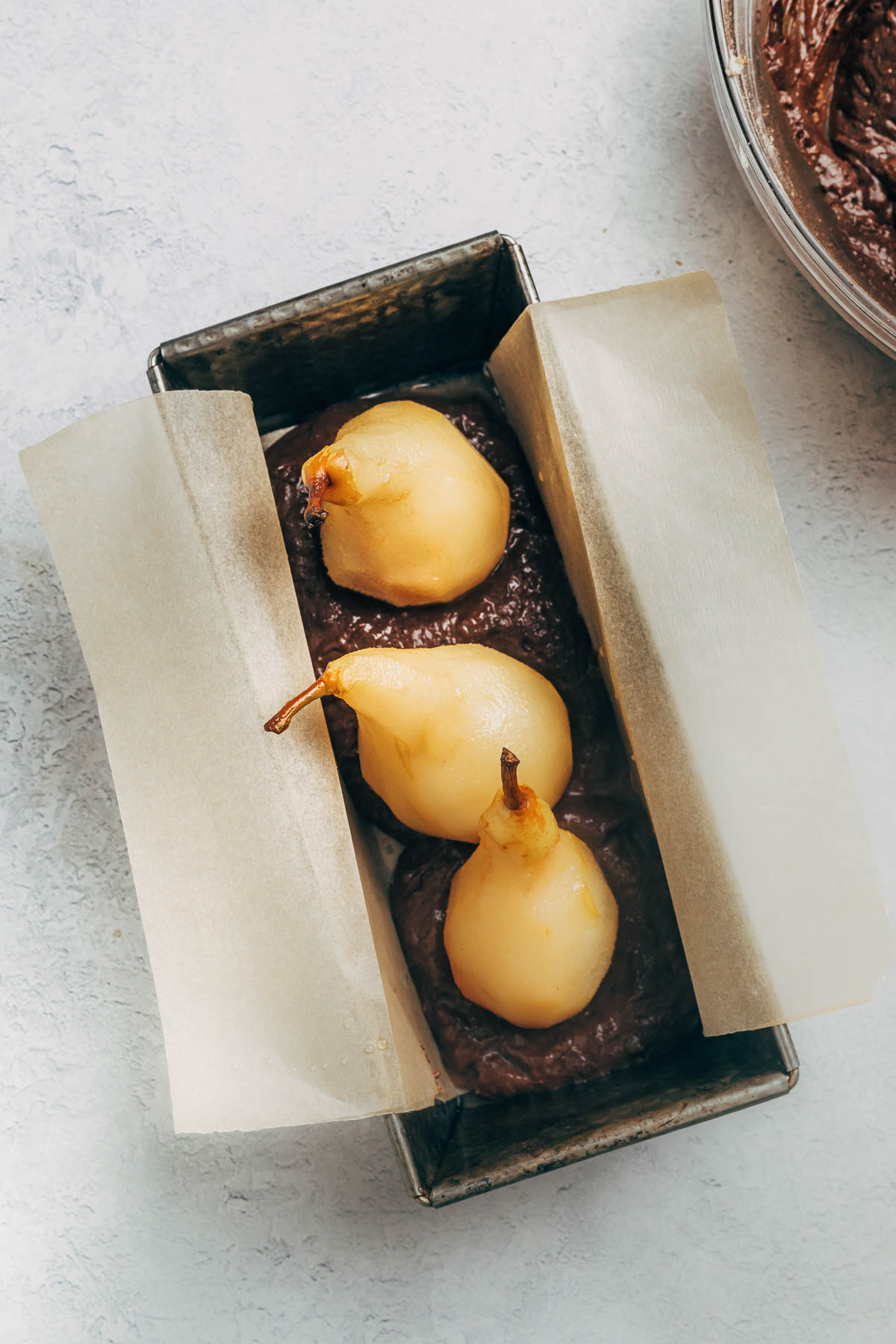 Overhead shot of whole poached pears and chocolate batter inside a loaf tin lined with parchment paper.