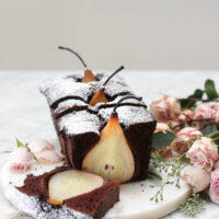 A sliced chocolate loaf cake on a marble platter with whole poached pears inside the loaf.