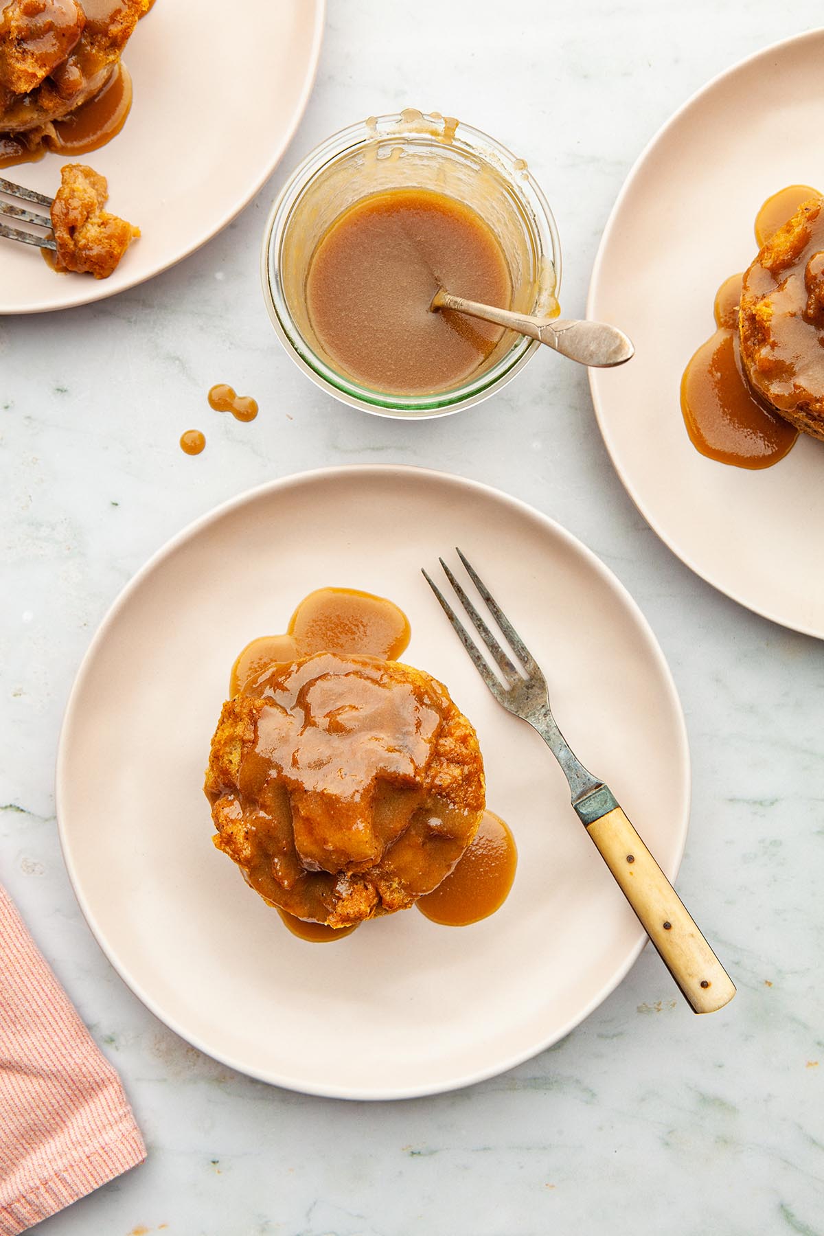Three servings of pumpkin bread pudding on plates, topped with butterscotch sauce.