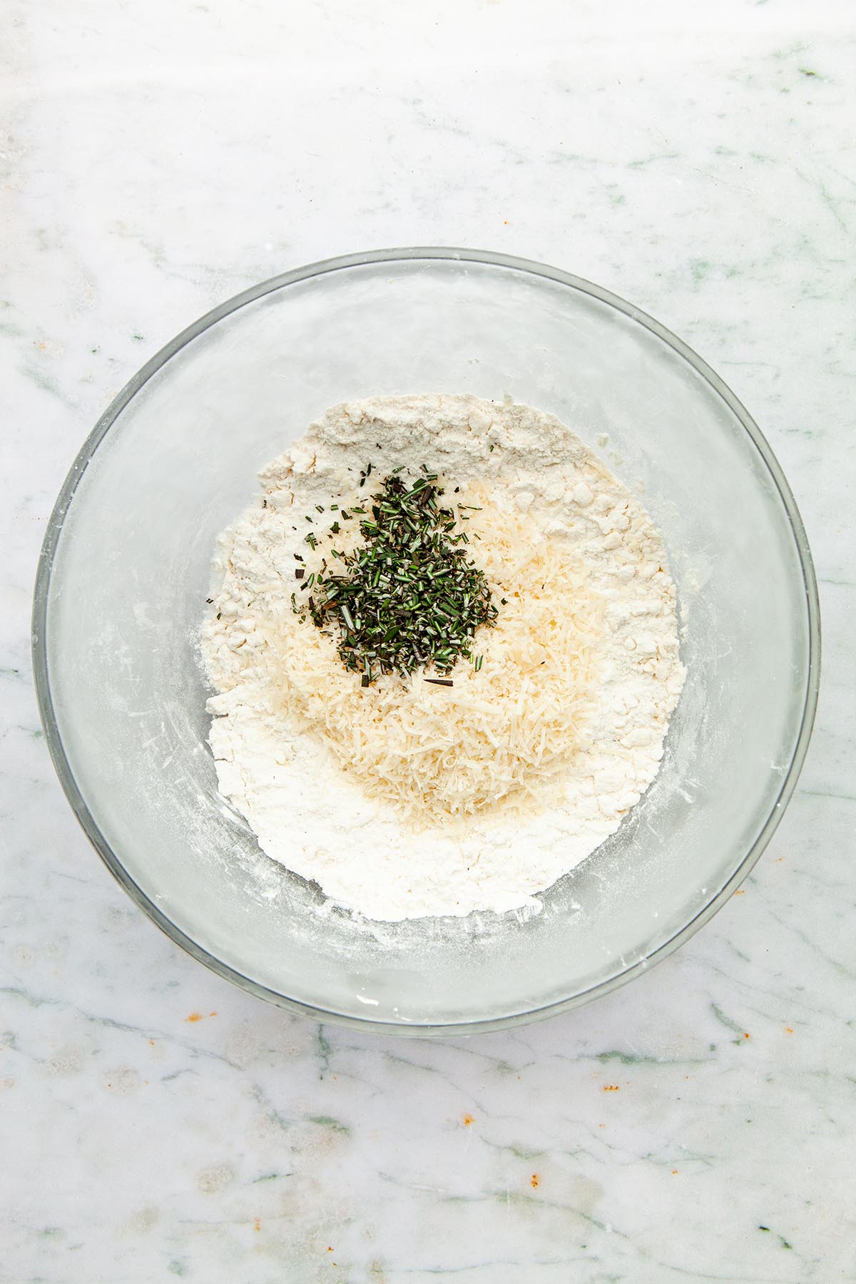 A bowl of flour with grated Parmesan & chopped rosemary on top.