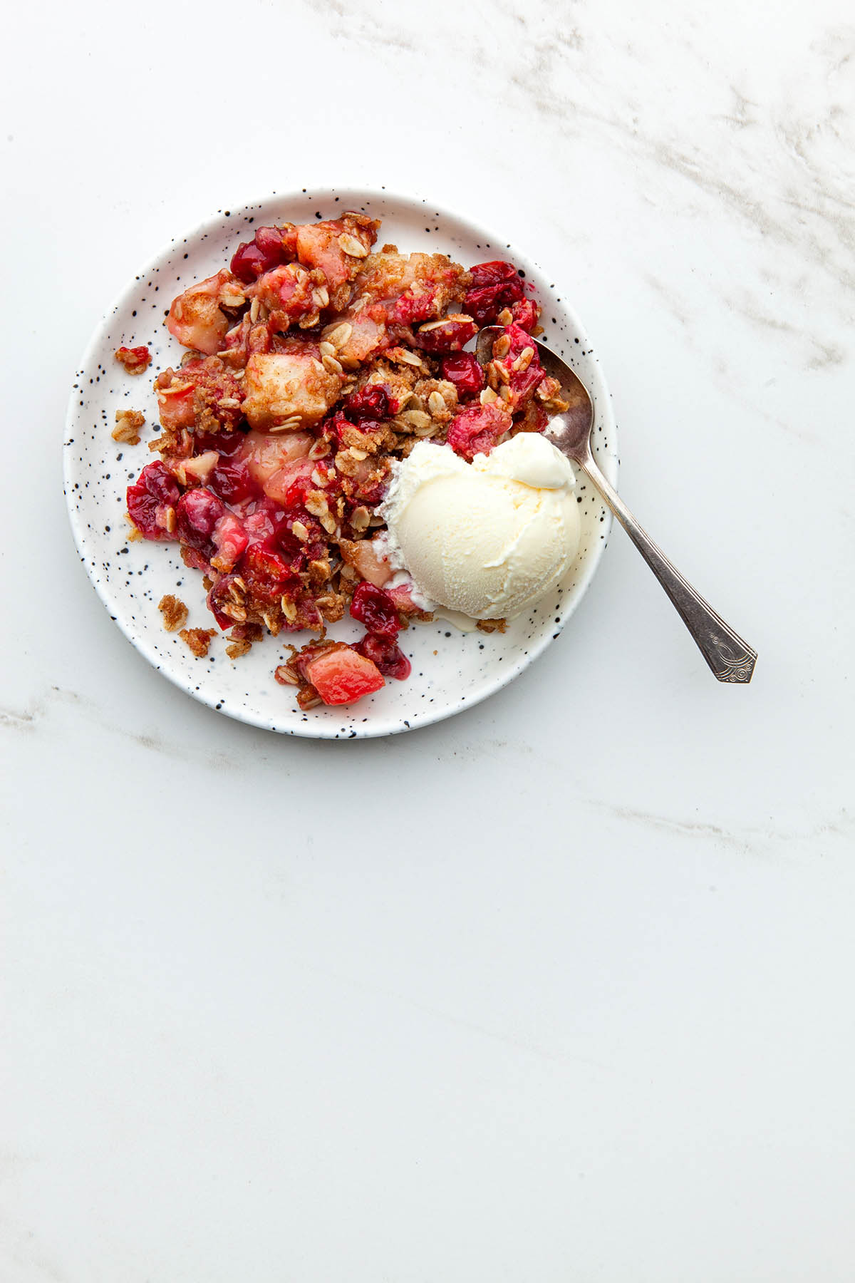 A plate of cranberry apple crisp topped with ice cream.