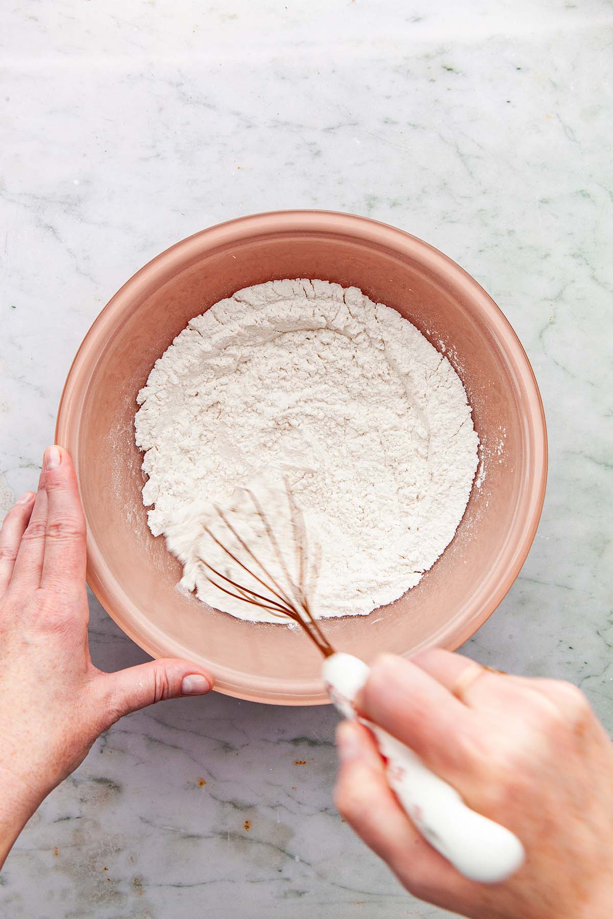 A hand whisking flour in a pink glass bowl.