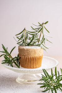 A vanilla cupcake topped with buttercream and rosemary trees on a small platter.